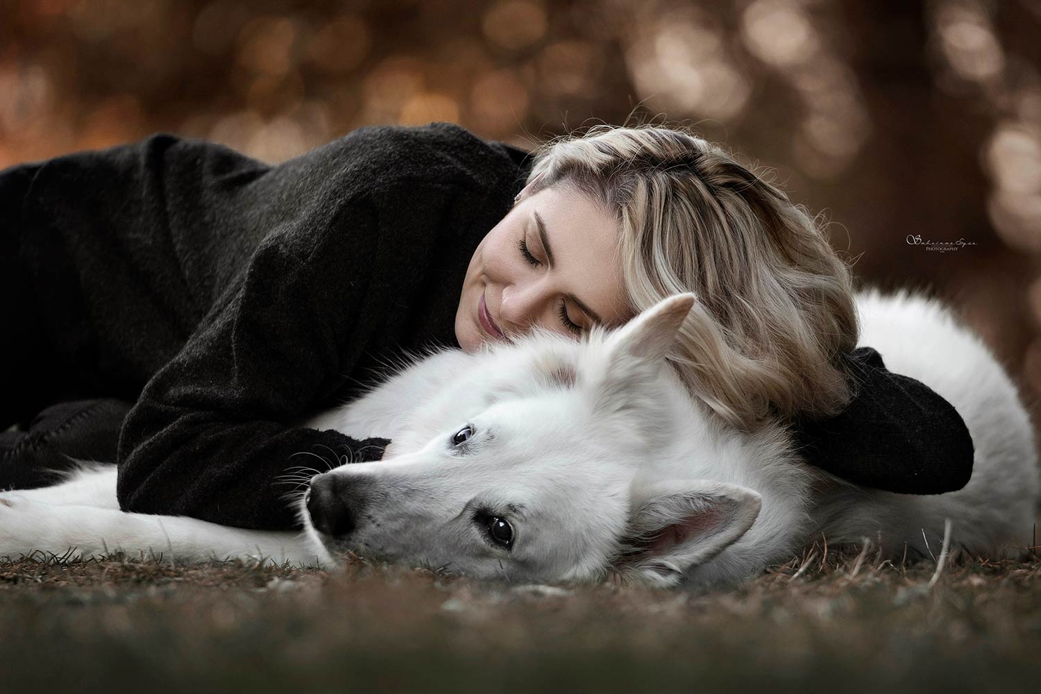 Eine Frau liegt auf dem Boden und kuschelt mit einem weissen Hund in einer herzlichen und friedlichen Szene.